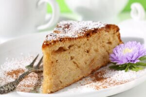 haselnuss-apfelkuchen mit staubzucker und blumendeko auf teller