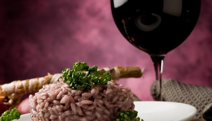 teller mit rotem risottoreis und einem glas rotwein